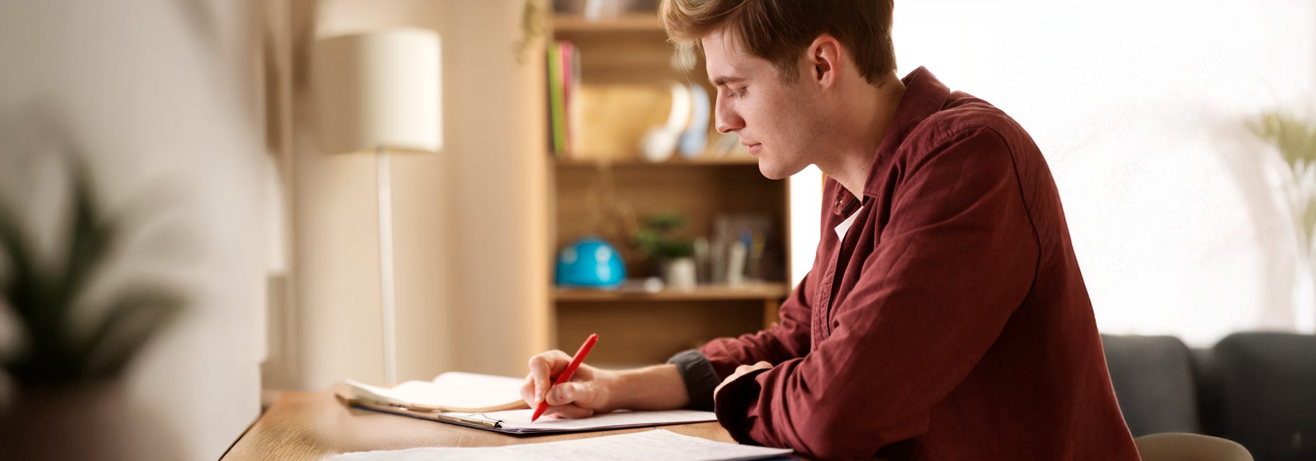 Junger Mann sitz an einem Tisch mit Stift und Papier